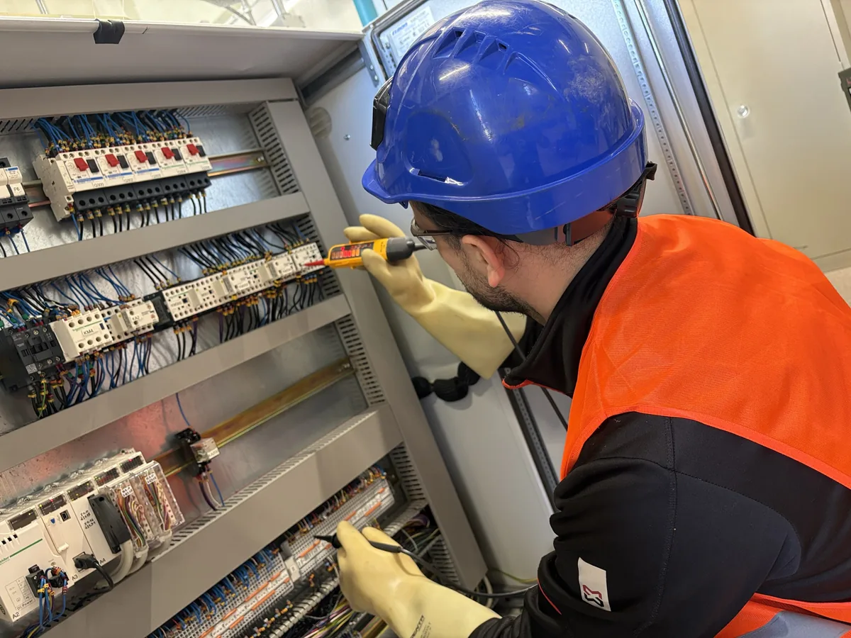 Intervention en armoire électrique basse tension : technicien casqué, gants isolants